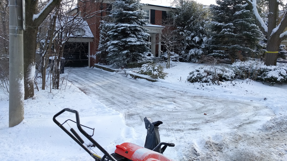 Snow blower in front of a home driveway just cleared of snow