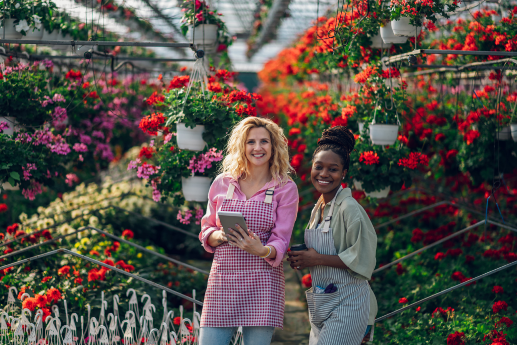 Two women in a nursery smiling, ready to assist with flower bed design questions