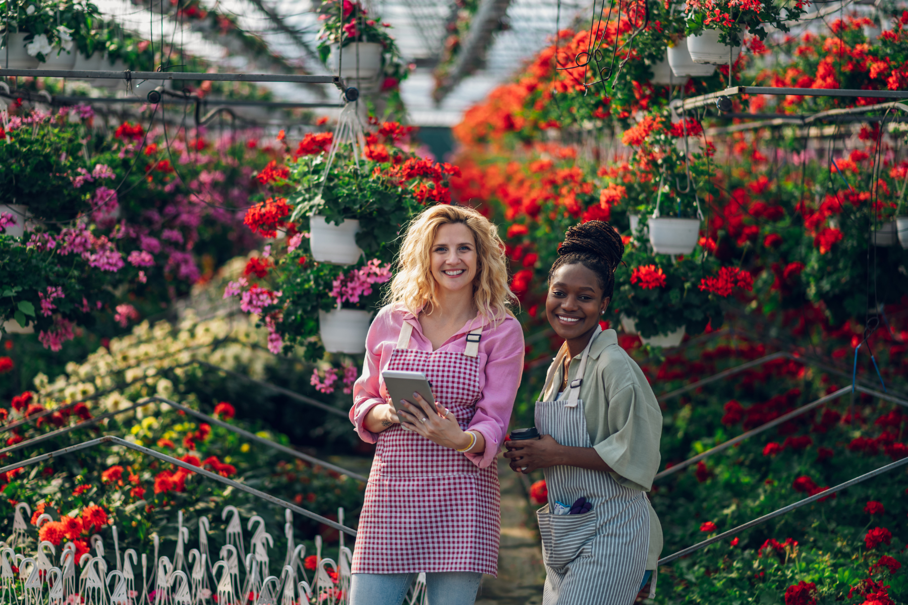 Two women in a nursery smiling, ready to assist with flower bed design questions